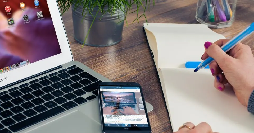 Person writing keyword ideas next to a laptop and phone