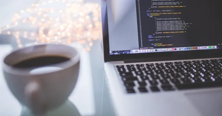 Laptop showing website code next to a coffee cup
